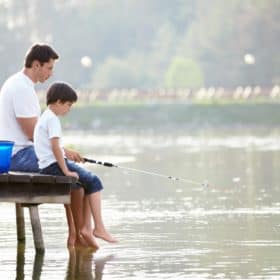 Father sitting and fishing on a dock with his son. Get our list of amazing gift ideas that EVERY father will love. Discover more parenting hacks and family lifestyle inspiration by following Made In A Pinch on Pinterest!