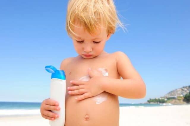 little boy on a beach rubbing sunblock on his tummy