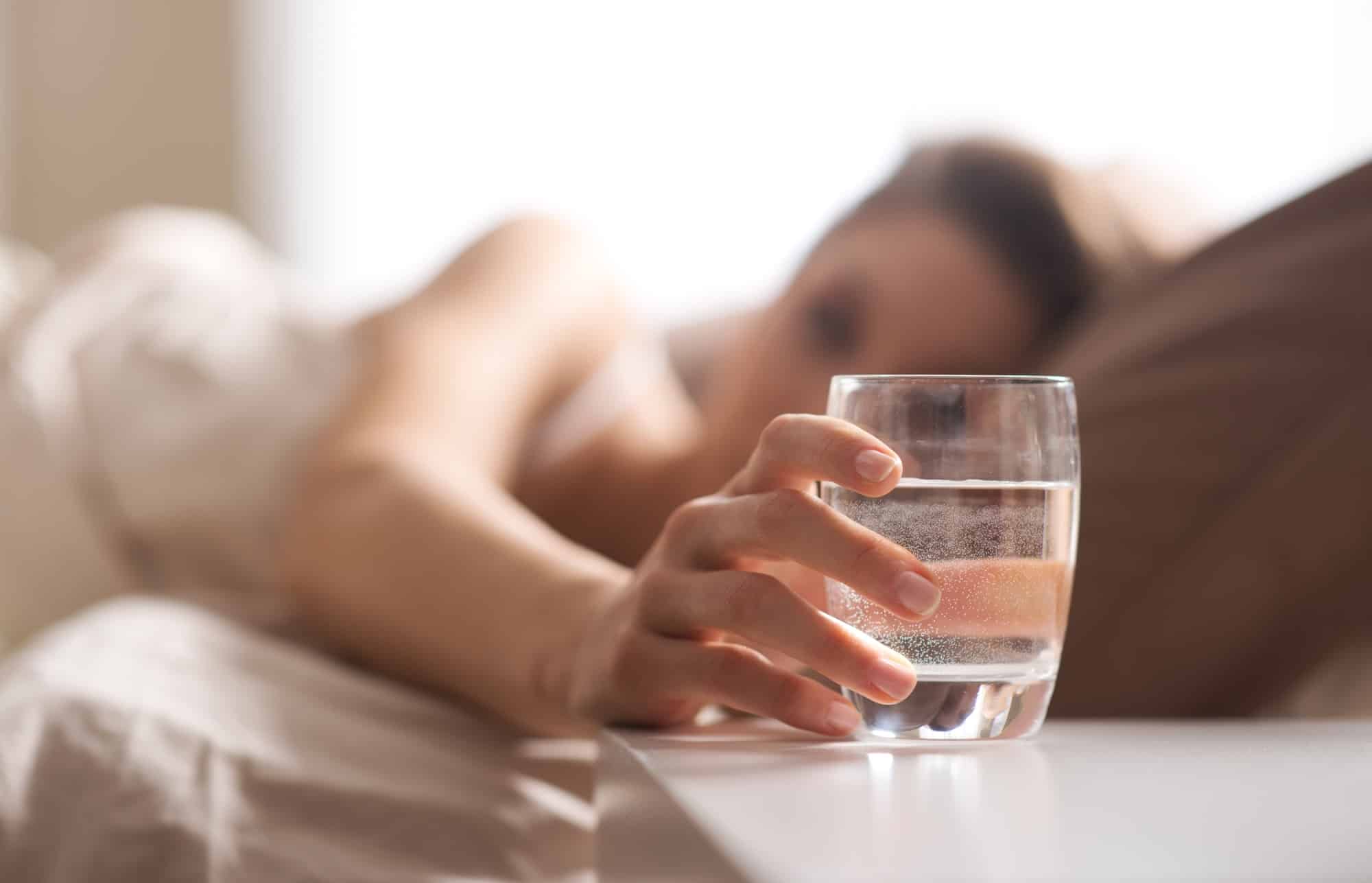 Woman reaching for a glass of water from bed so she can drink more water
