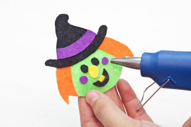 Witch Halloween bookmarks craft for kids tutorial, Gluing on the purple strip for the hat, the eyes, nose, mouth, and dimples