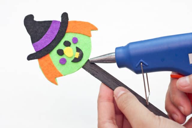 Witch Halloween bookmarks craft for kids tutorial, hot gluing the witch's head to the popsicle stick