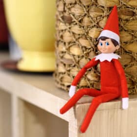 Elf on the shelf sitting on a shelf is part of this mega list of elf on the shelf ideas for toddlers that any busy, tired mom can do