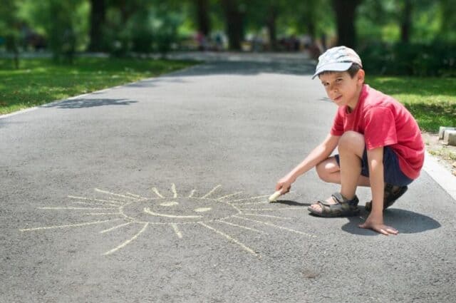 Little boy drawing a sun with chalk on the sidewalk, just one of 14 ideas of fun games to play when bored at home