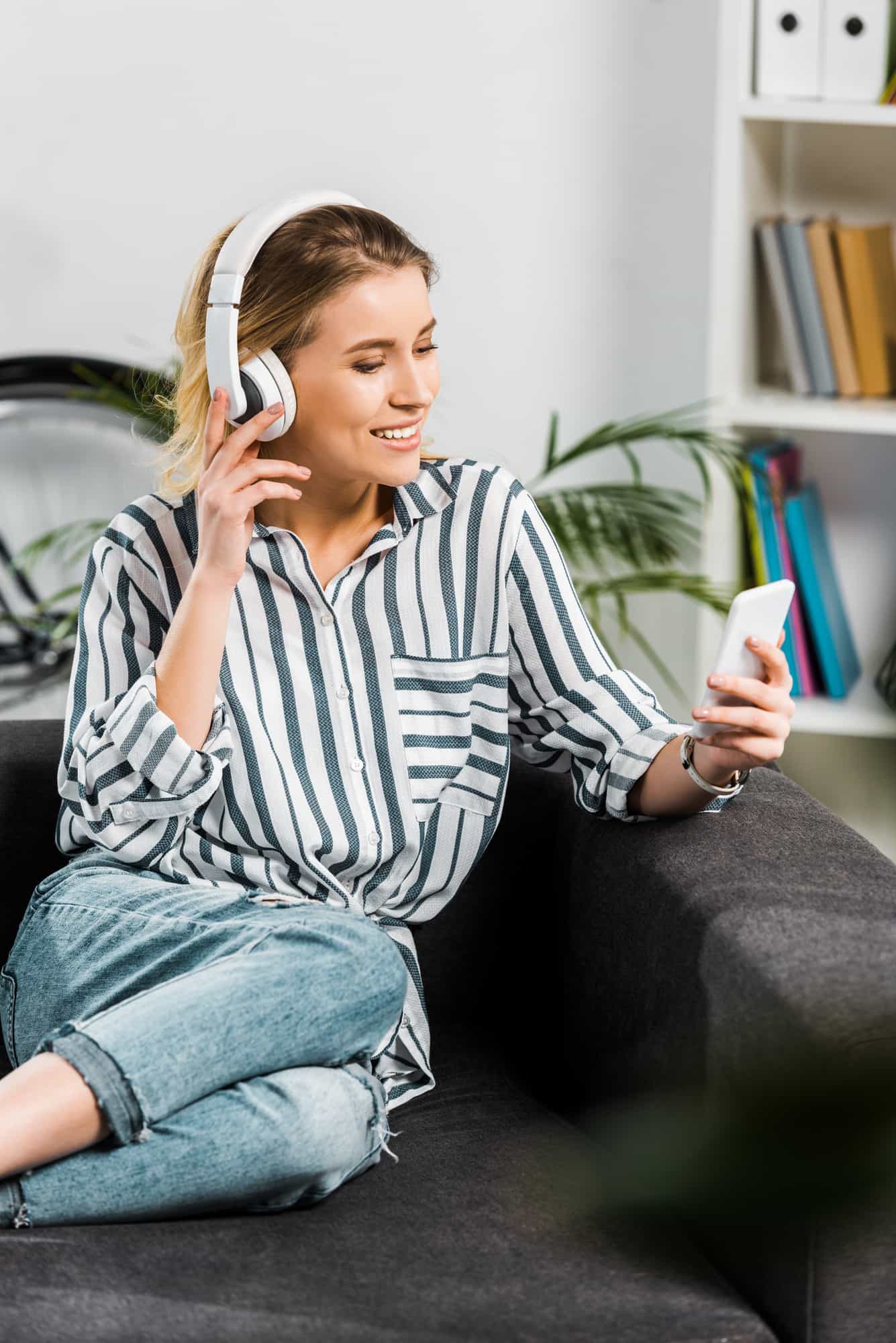 woman sitting on couch with headphones listening to podcast