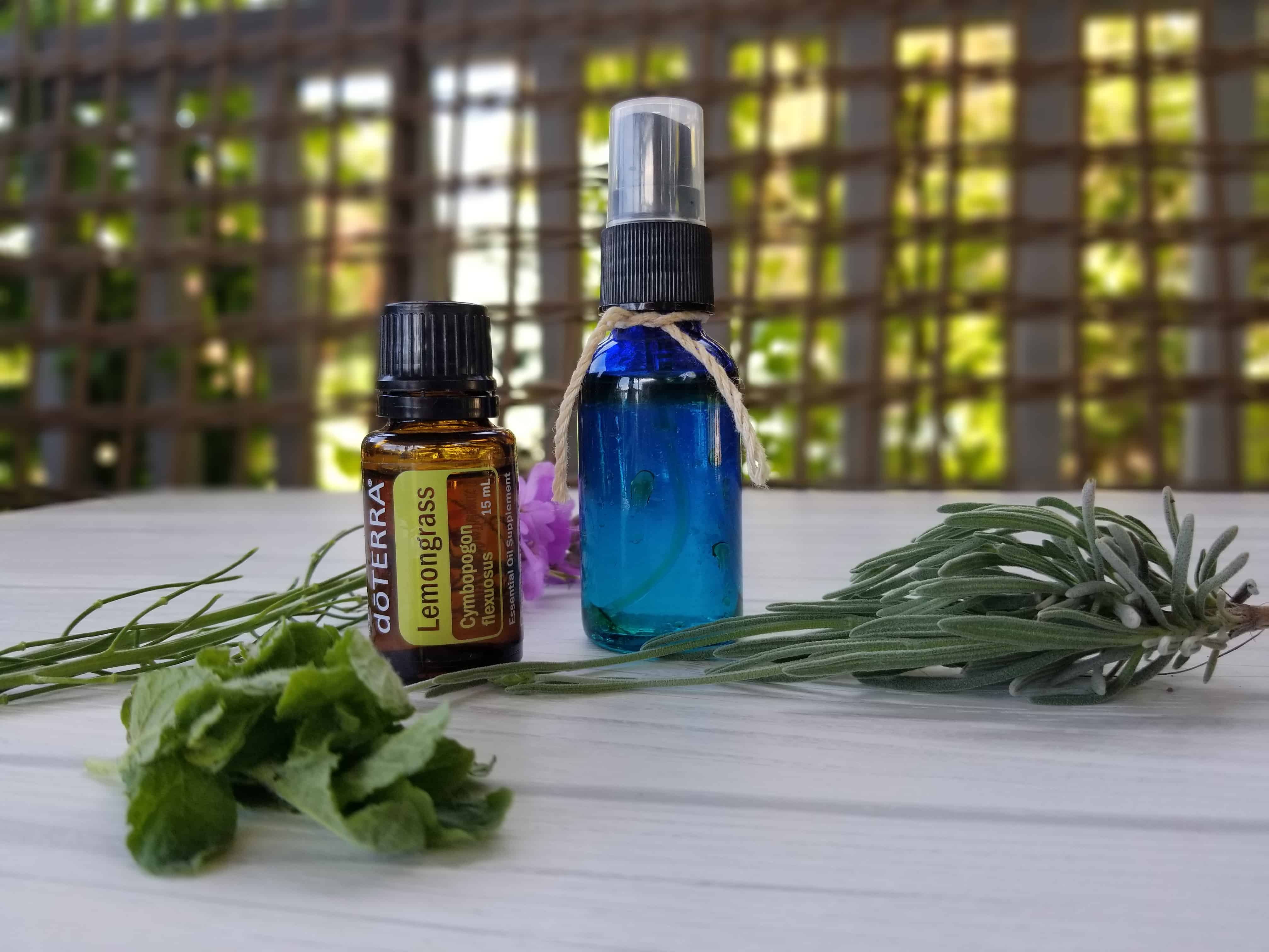 blue spray bottle with essential oil mosquito repellent, lemongrass essential oil bottle and greenery