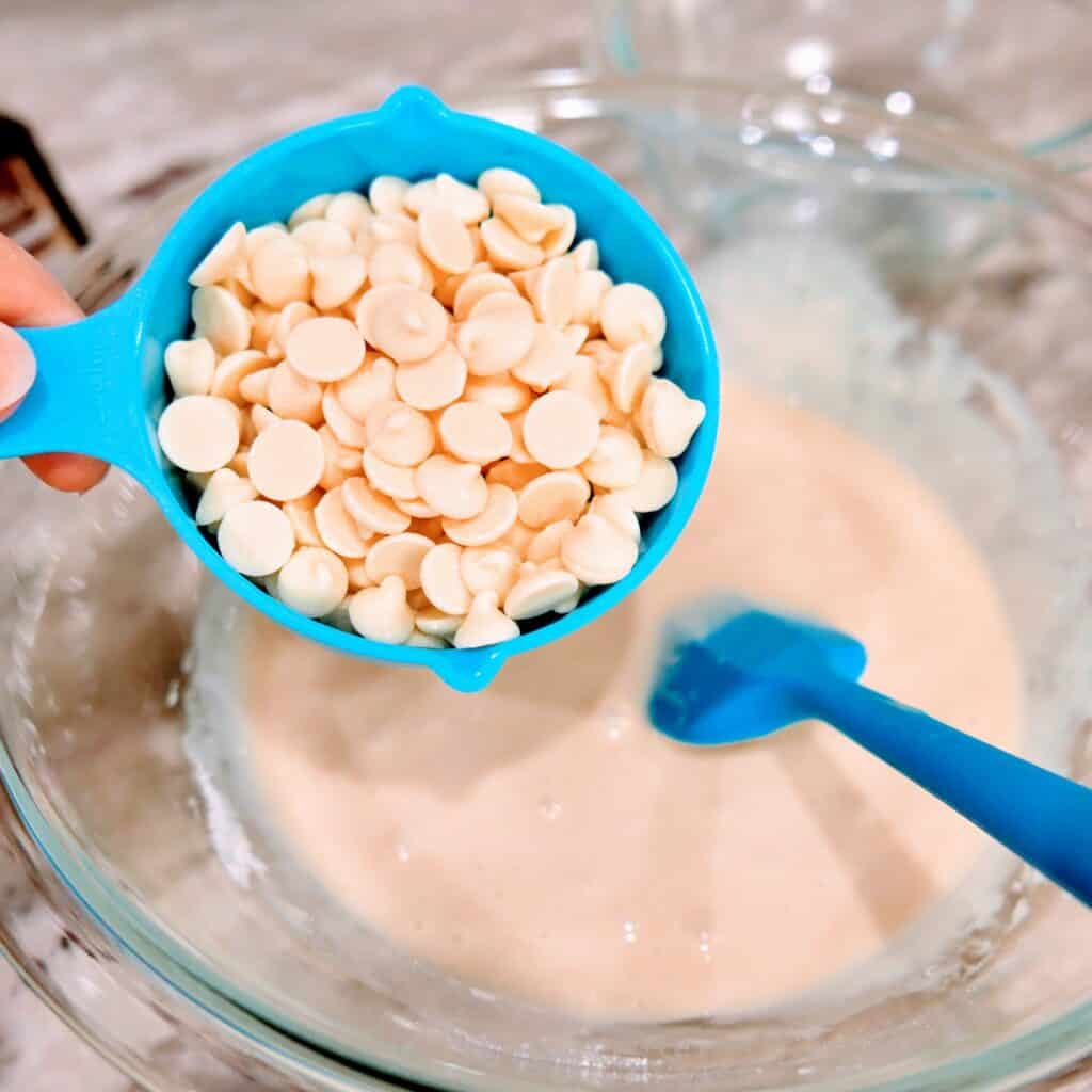 adding white chocolate chips to a bowl with sweetened condensed milk in it