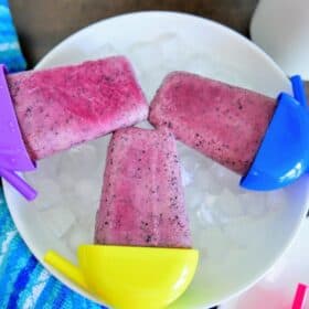 3 blueberry popsicles on a bowl of ice