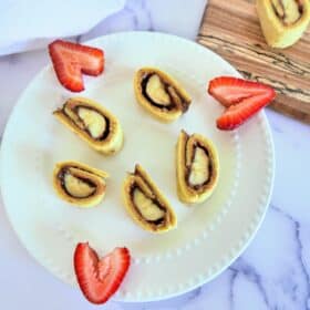 sliced banana sushi rolls on a plate with cut up strawberries