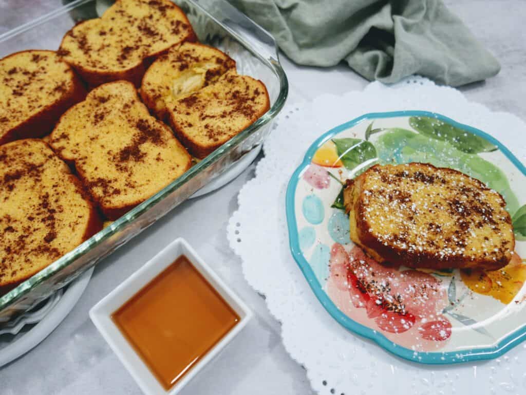 pan of pumpkin french toast with a piece on a plate and a side of maple syrup.