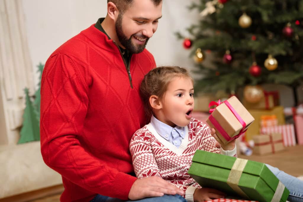 dad sitting with girl as she's opening holiday gifts