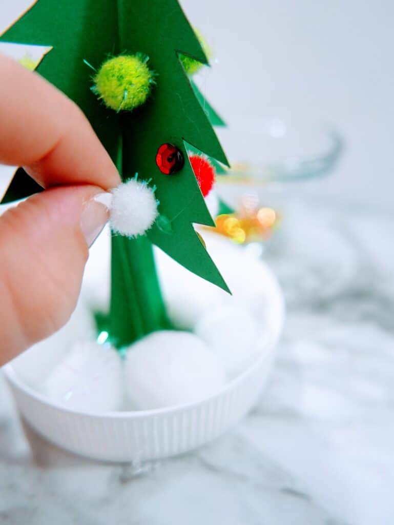 gluing poms and sequins onto the tree for the inside of the homemade snow globe