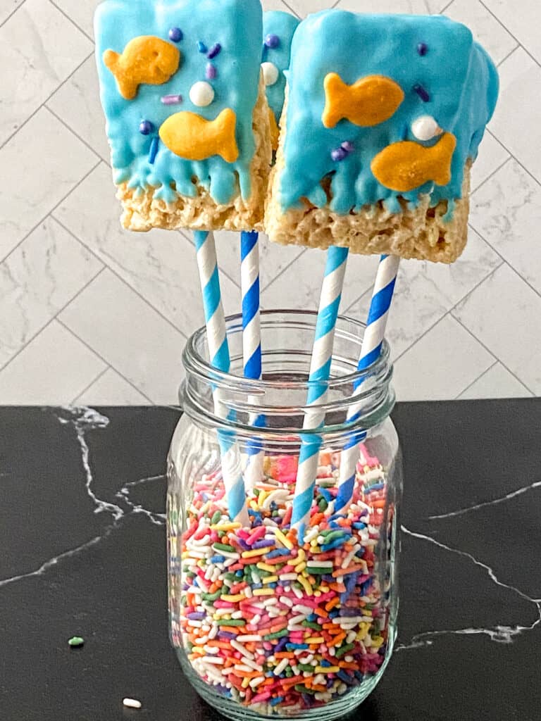 blue coated rice krispie snacks on sticks in a jar
