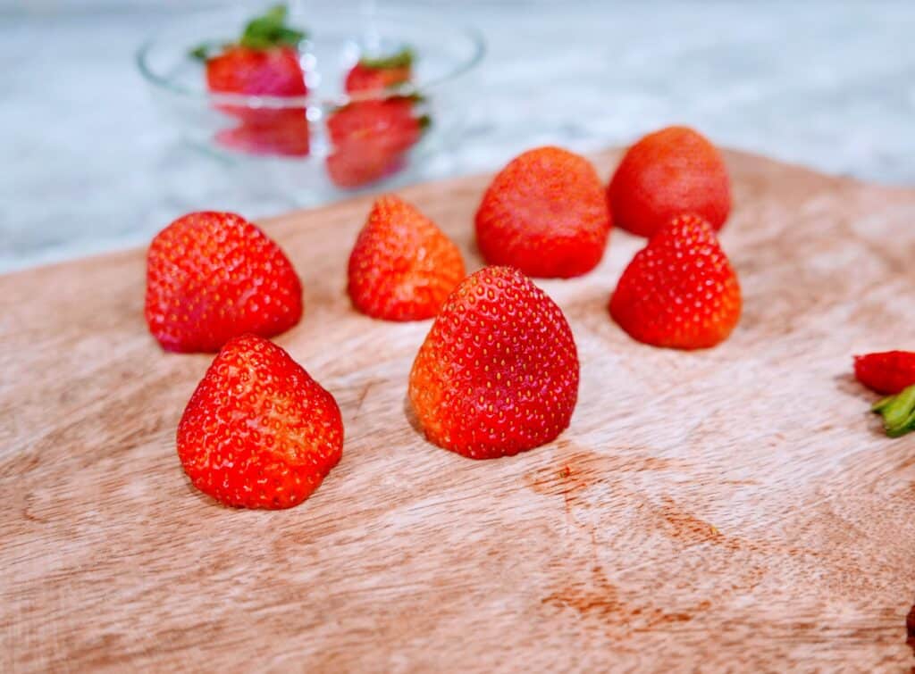strawberries with their tops cut off on a cutting board.