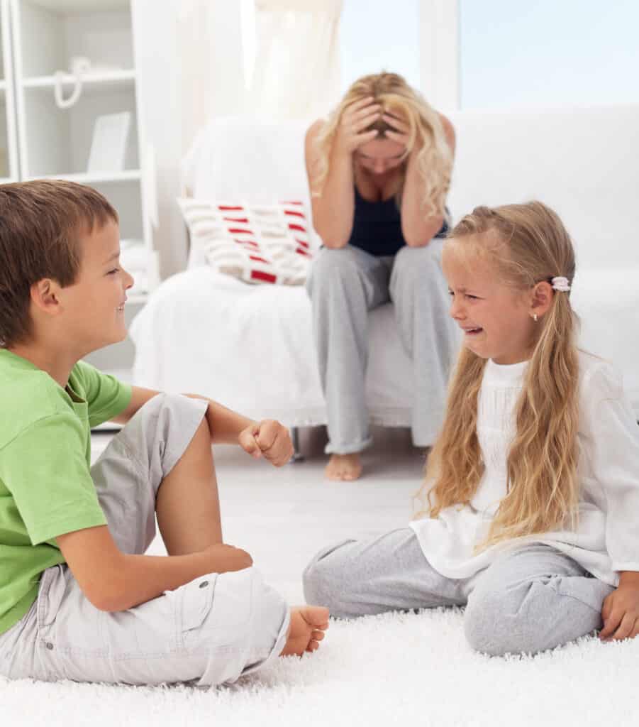 Exasperated mom sitting on couch while little boy and girl fight and cry
