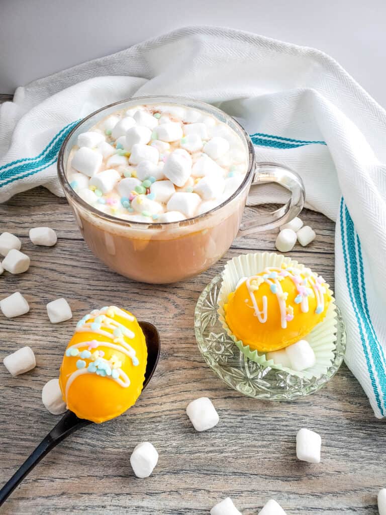 Easter egg hot cocoa bombs with mini marshmallows scattered around