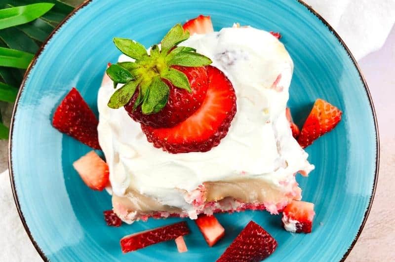slice of strawberry cheesecake poke cake with fresh strawberries