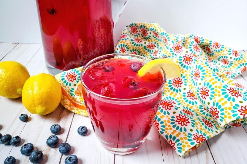 glass of blueberry lemonade with lemons and blueberries