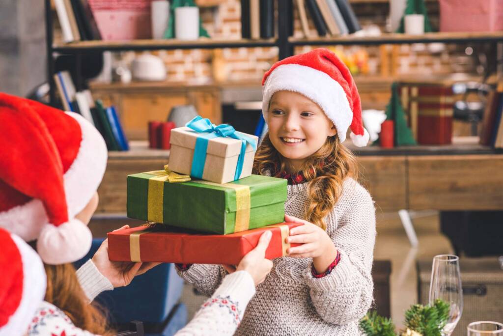little girl wearing a Santa hat and giving gifts - how to talk to kids about Santa