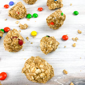 Homemade Chocolate Peanut Butter Energy Balls with colorful candies scattered around on a light wooden surface.
