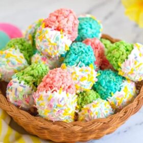 Colorful Easter Egg Rice Krispie treats dipped in white chocolate and sprinkled with rainbow sprinkles, arranged in a wicker basket.