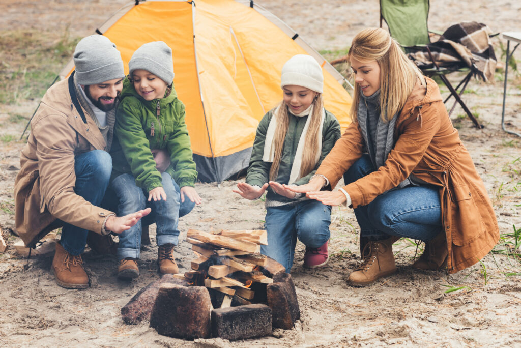 family warming hands by fire wearing car camping essentials