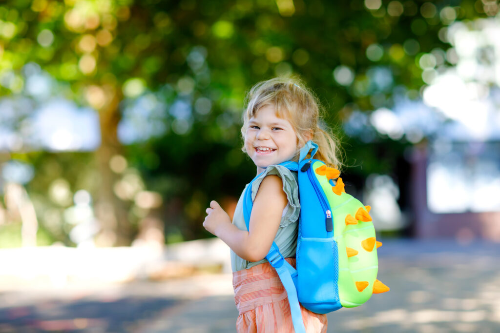 little girl wearing backpack for preschool and smiling at the camera