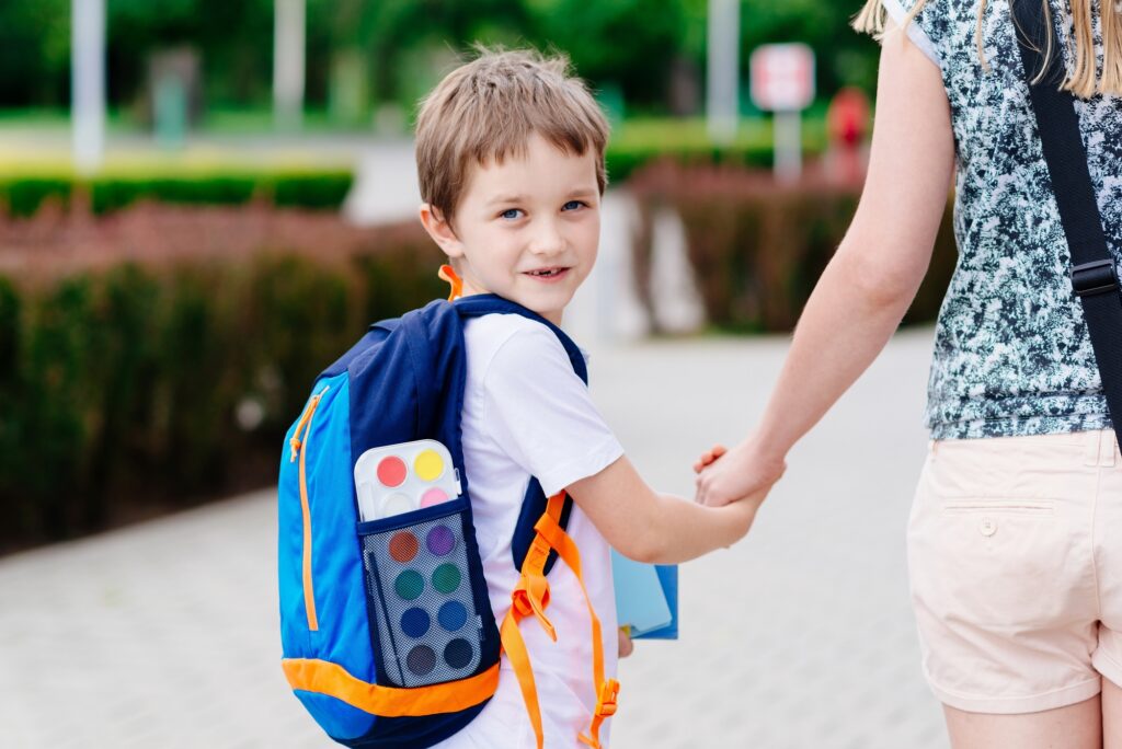toddler boy wearing a pre-k backpack and holding his mom's hand