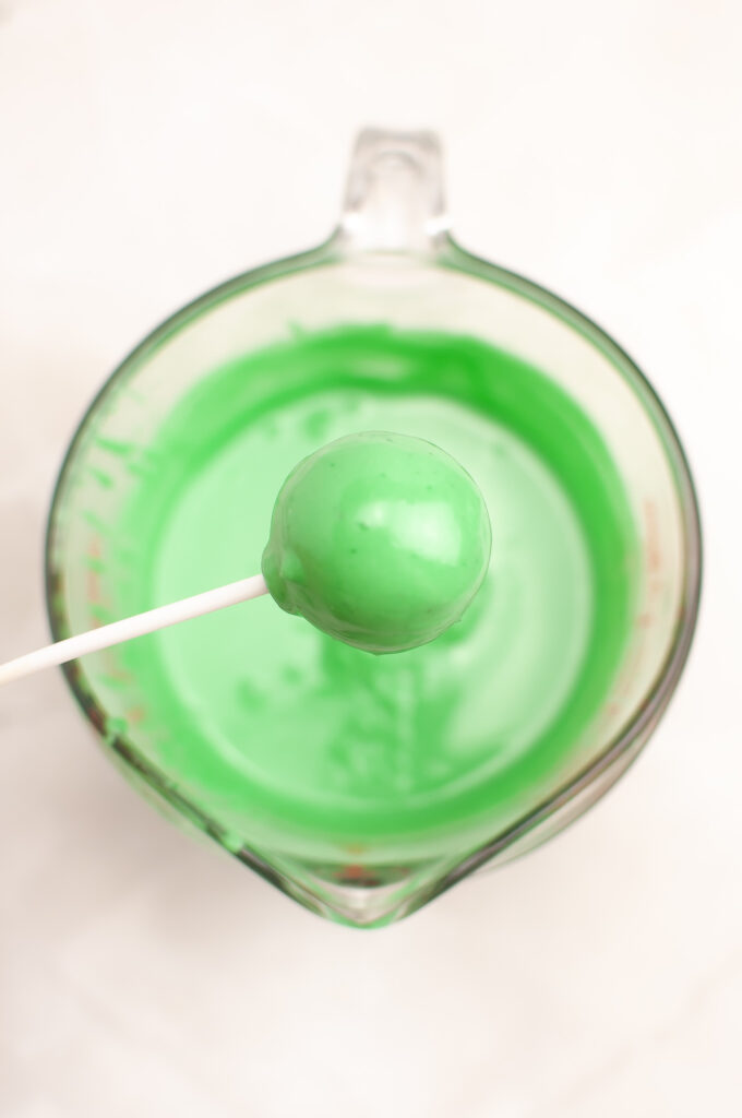 dipping Grinch cake pop into melted green chocolate