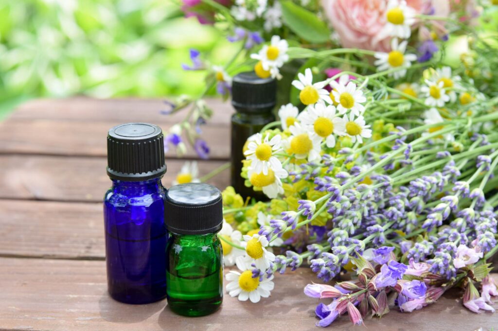 A blue bottle and green bottle of essential oils with flower blossoms