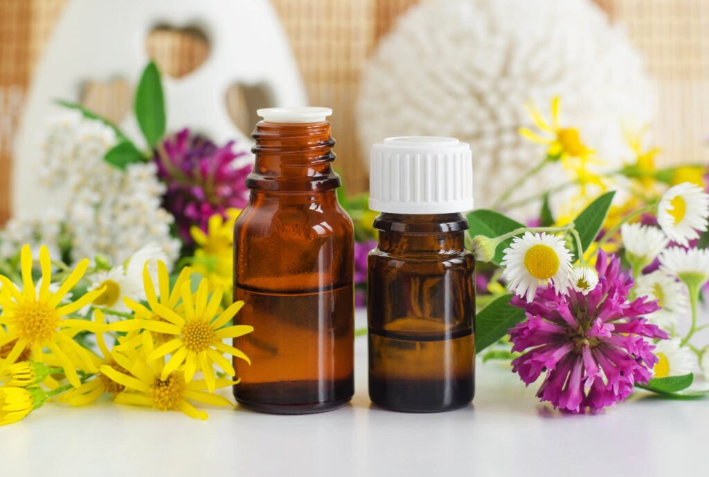 Two bottles of essential oils standing surrounded by yellow and purple flowers