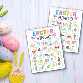 Two Easter bingo cards displayed on a light wooden table alongside colorful Easter eggs and a yellow bunny decoration.