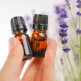 Lavender essential oil in brown glass bottles in a female hand and lavender flowers on a white background.
